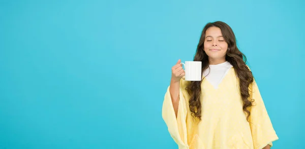 Roztomilá holka drží šálek kávy. Dobré ráno. Malá modrá dětská zeď. Holčička pije kakaové mléko před spaním. Útulné načechrané pyžamo. cítit se jako doma. kopírovat prostor. šťastná dívka s šálkem čaje — Stock fotografie