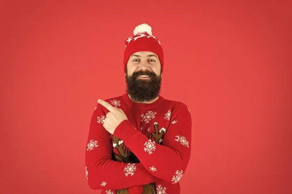 Зрілий бородатий чоловік оленячий светр. жорстокий хіпстер на в'язаному капелюсі червоний фон. носіть різдвяний настрій. в'язаний одяг чоловічої моди. смішний чоловік, який вказує пальцем. досі вірять у Санта Клауса — стокове фото