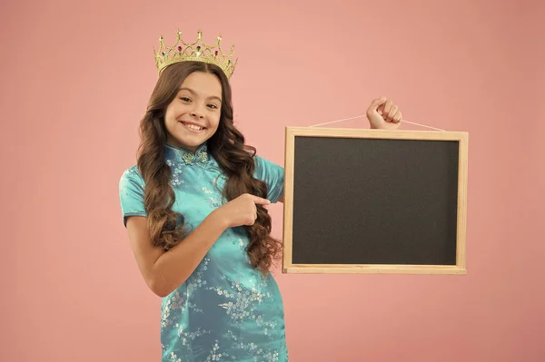 best offer here. Proud girl in crown back to school. Empty board for promo or advert, copy space. Small child wear prom crown. Holiday celebration in school. Happy princess hold school blackboard