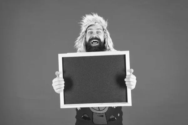 Marketing and advertising. Happy hipster hold empty blackboard. Bearded hipster in winter wear. Hipster with mustache smile. Brutal hipster with advertising board, copy space — Stock Photo, Image