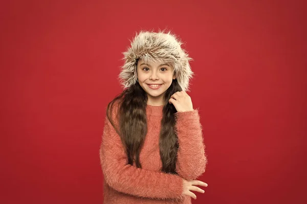 Ζεστό καπέλο για κρύο χειμώνα. Μικρό κορίτσι κόκκινο φόντο. Μαλακό γούνινο αξεσουάρ. Χειμερινή περίοδος. Σχέδιο αγορών. Κράτα το κεφάλι σου ζεστό. Ζεσταίνομαι. Παιδικό μακρυμάνικο καπέλο. Χειμερινή μόδα έννοια — Φωτογραφία Αρχείου