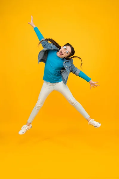 Feliz saltando menina adolescente com cabelos trançados usar óculos para a visão no fundo amarelo, de volta à escola — Fotografia de Stock