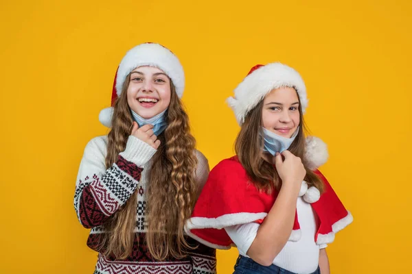 Fira vinterlov i karantän. Julshopping på nätet. Vänskap mellan tonårsflickor. försäljning av presenter och presenter. Glada tomtebarn. leende barn i tomte hatt och skyddsmask — Stockfoto