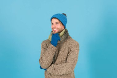Kaygısız ve mutlu. Tıraşsız yakışıklı adam mavi arka planda kış aksesuarları takıyor. Kış sezonu indirimi. Hippi, kış şapkası eşarbı ve eldiven ördü. Alışveriş konsepti. Duygusal ifade