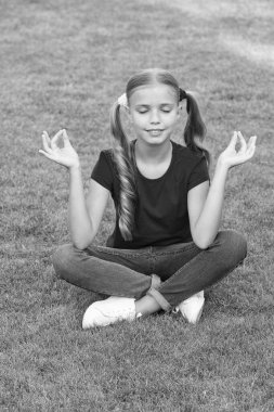 Meditasyon pratiği. Küçük çocuk yeşil çimenler üzerinde meditasyon yapıyor. Küçük kız meditasyon sırasında Mudra pozisyonunda oturur. Yoga meditasyonu. Zen ve aydınlanma. Yaz tatili. Konsantrasyon için meditasyon yap