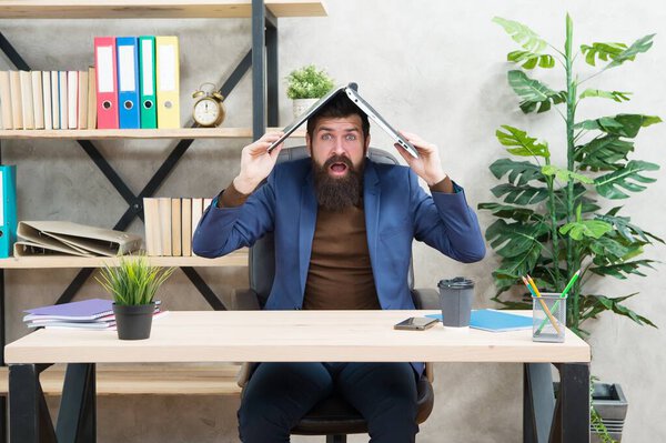 Bearded man in formalwear hold laptop computer on head keeping eyes and mouth open at workplace in modern office, shock