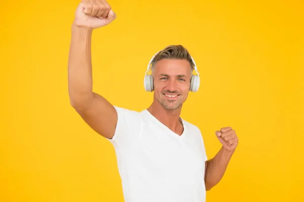 Gelukkige energieke man luisteren naar muziek in hoofdtelefoon maken winnende gebaar gele achtergrond, overwinning — Stockfoto