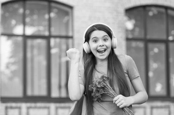 Richtige Art zu feiern. Glückliches Kind macht Siegergeste. Kleines Mädchen hält Blumen in der Hand und hört Musik. Jubiläumsfeier. Geburtstagsfeier. Feiertagsfeier. Es ruft zum Feiern auf — Stockfoto