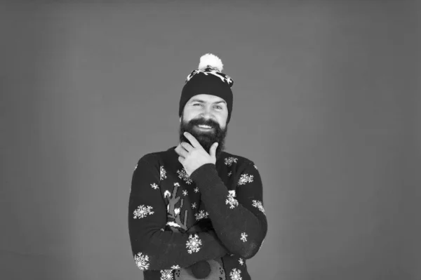 Bearded face close up red background. Cold days. Winter holidays. Man bearded hipster wear winter knitted hat. Barbershop and facial hair. Winter skin care. Guy wearing winter clothes and accessory