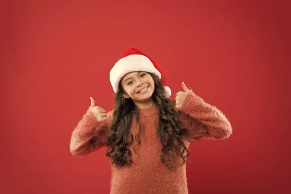 Boas férias. férias de inverno favorito. a divertir-se. Pequeno Pai Natal. sentir-se feliz com o ano novo. tempo para o feriado de Natal. Menina pequena em chapéu de santa. parede vermelha criança alegre. inverno criança moda — Fotografia de Stock