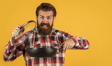 Öğle yemeği vakti. Mutfaktaki aşçıda tencereyi pişirirken. Yemek hazırlamak ve yemek pişirmek. Mutfak aletleri. Mutfak reklamı. Tencereli adam. Adam yeni marka tavayı tutuyor. Mutfak gereçleri