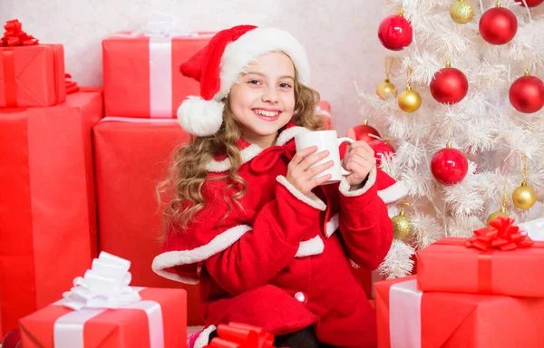 Chapeau de père Noël enfant profiter de boisson au cacao. Parfait moyen de vous réchauffer pendant les fêtes. Chocolat chaud le soir de Noël. Boisson préférée de cacao. Petite fille mignonne enfant tenir tasse avec boisson chaude tout en célébrant Noël — Photo