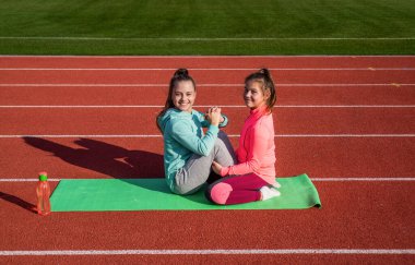 En iyi olmak için eğitim. Çocuklar yolda egzersiz yapar. sağlıklı çocukluk. Temiz hava egzersizi. Susuzluk ve susuzluk. Genç kızlar stadyumda bilek güreşi yapıyor. Spor giyimli çocuklar yoga minderinde rahatlar.