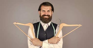 O çok mutlu. Resmi yelek giymiş yakışıklı bir adam. İş modası için gardırop. Giysi ve alışveriş. Askıda asılı duran şık erkek kıyafetleri. Terzi elinde bir askı tutuyor.