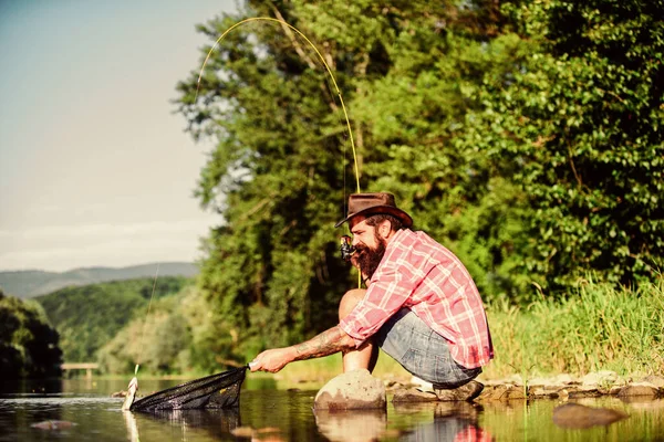 Hipsterskie łowienie z przynętą na łyżki. Dojrzały brodaty mężczyzna z rybą na wędce. odnoszący sukcesy rybak w wodzie jeziora. hobby dla ryb muchowych. Aktywność letnia. Łowienie ryb. zrelaksować się na łonie natury. To jest wielka ryba. — Zdjęcie stockowe