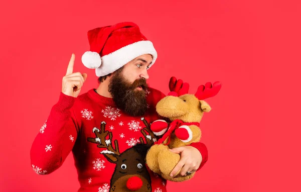 Lost in Christmas thoughts. Christmas party man with reindeer toy. happy guy await new year present. lets have fun. Santa Claus hipster. handsome man at Christmas. brutal bearded male red background — Stock Photo, Image