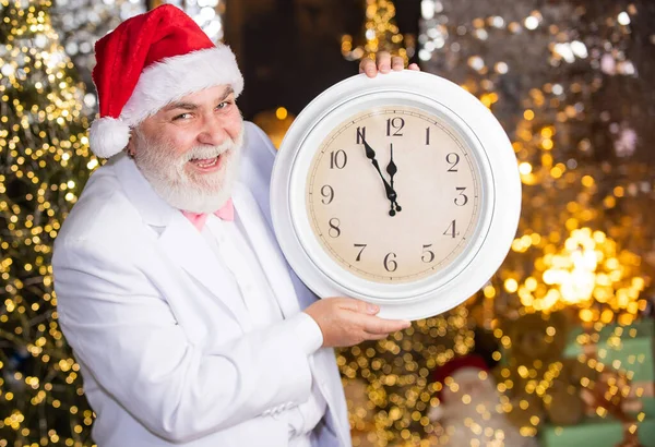 新年のカウントダウン。レトロな時計の男。ガーランド照明の背景。サンタの帽子の髭のビジネスマン。タキシード姿のサンタさん。クリスマス・イブ。サンタは時間を数える。真夜中のコンセプト — ストック写真