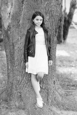 Sevimli ve modaya uygun. Parktaki ağaçta duran küçük çocuk. Küçük modelin modası geçti. Tasarımcı çocuk giyimi ve giyimi. Moda ve tarz. Çocuk modası ve yaşam tarzı. Moda eğilimi