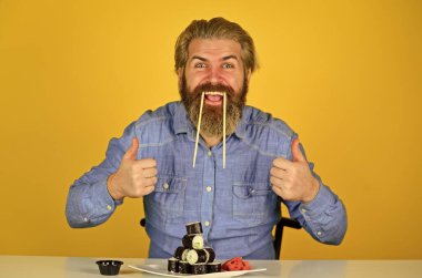 Asya yemeği. Suşi siparişi. Adam evde suşi yiyor. Çubuklu suşi ve zencefil. Japon mutfağı. Doğu kültürü. Sakallı hippi rulo yiyor. Japon yemek teslimatı. Suşi rulo