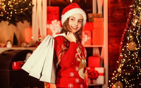 Papai Noel carrega presentes de Natal. compras de presentes de férias. Está na hora do Natal. O ano novo está chegando. Camisola de rena infantil e chapéu de Pai Natal. sacos de compras e pacotes para a família. pequeno shopaholic — Fotografia de Stock