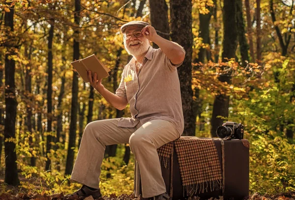 Mature man with white beard in forest. Hobby and leisure. Grandfather with vintage suitcase in nature. United with nature. Weekend in nature. Vacation and relax. Retirement concept. Elderly people