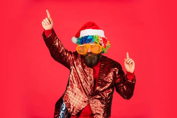 Brodatego hipstera w świątecznych okularach. Człowiek z brodą w czapce Świętego Mikołaja. Brutalne, czerwone tło. Świąteczne zakupy online. Impreza zimowa. Dojrzały facet świętuje Nowy Rok. Dla Mikołaja — Zdjęcie stockowe
