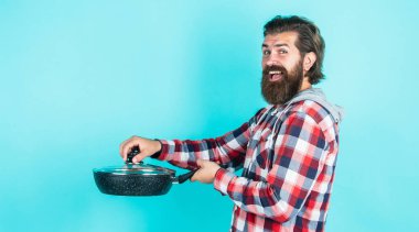 Neredeyse hazır. Şık erkek yemek pişirecek. Bıyıklı sakallı adam mutfak aletleri kullanıyor. Sağlıklı yemek. Yapışmayan yüzey. Şef yemek yapıyor. Tavalı, kareli gömlekli olgun bir adam.