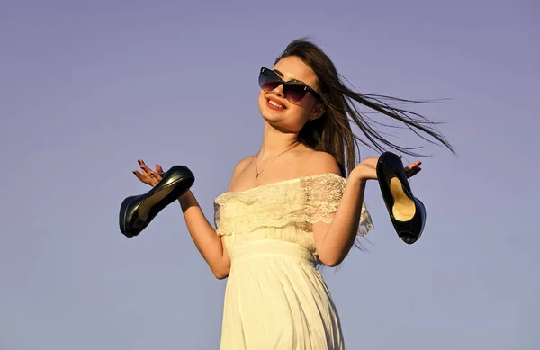 Mulher no céu azul ensolarado da manhã. Férias de verão. Modelo tenra vestido de verão. Liberdade. Menina em óculos de sol espaço de cópia. Para o verão. Conceito de Afterparty. Mulher nascer do sol carregam saltos altos na mão — Fotografia de Stock