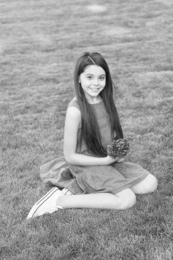 Rahatla, gevşe ve kendini bırak. Mutlu çocuk yeşil çimlere oturur. Çocuk kızın güzel görünüşü. Uzun saçlı, sıradan bir çocuk. Yaz modası trendleri. Çocuk bakımı ve çocukluk. Çocuk Günü