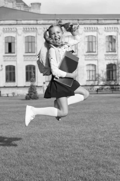 Salto menina bonito com notebook. menina pré-escolar feliz com livro no quintal da escola. de volta à escola. criança trabalhadora levar mochila. conceito de educação. férias de primavera. férias de verão — Fotografia de Stock