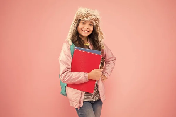 Förvänta dig det bästa. Tillbaka till skolan. vintersemester och semester. unge varma kläder rosa bakgrund. elev vardag.skolflicka bär ryggsäck och böcker går hem. Inga fler prov. lycklig flicka öronlapp hatt — Stockfoto