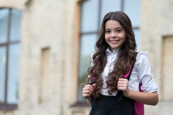 Счастливый ребенок носить длинные восые волосы со спиной к школе взгляд в школьном дворе, салон, копировальное пространство — стоковое фото