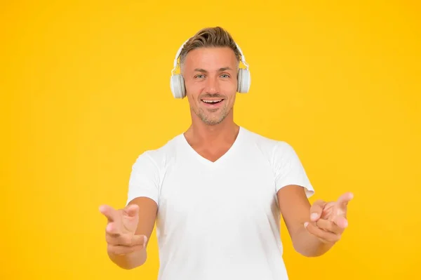 Homem de meia-idade feliz em fones de ouvido apontar dedos promovendo produto ou serviço fundo amarelo, apontando — Fotografia de Stock