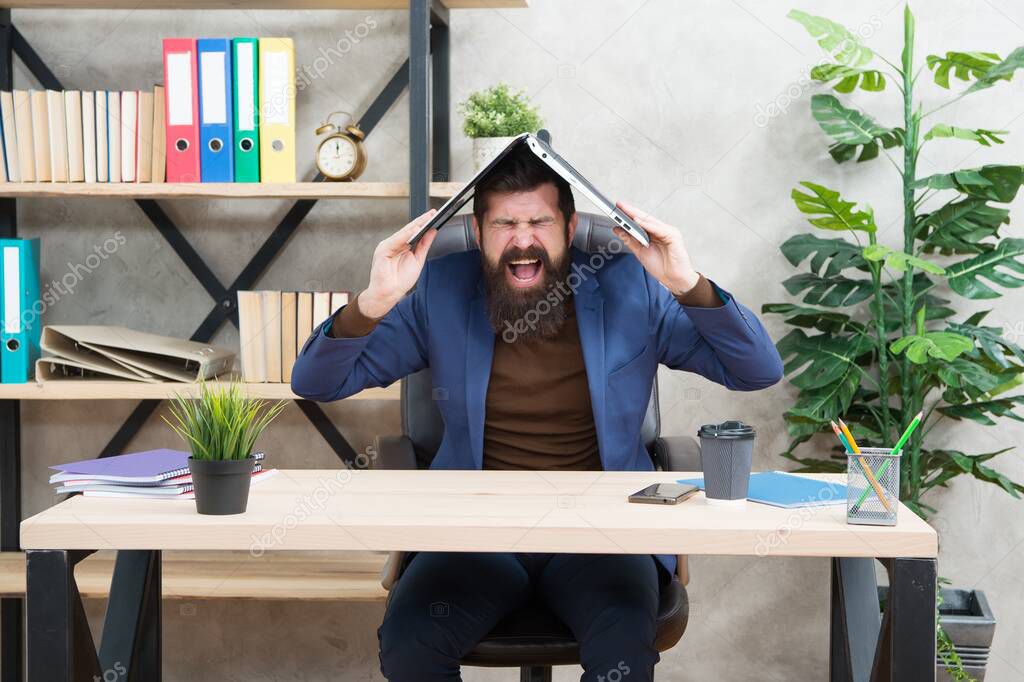 Troubled engineer scream in anger holding laptop computer on head in modern office, problem