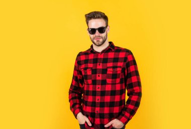 Havalı ve seksi. İyi bakımlı bir saç stili. Erkek güzellik ve moda. Sakallı adam için kareli gömlek. Tıraşsız, güneş gözlüklü yakışıklı adam. Kuaför konsepti. Genç ve kendinden emin