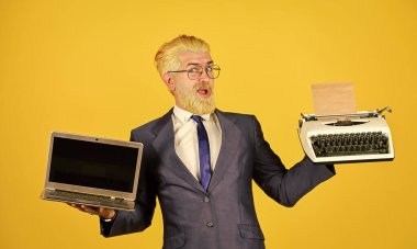 Dizüstü bilgisayara karşı daktilo. İş adamı modern teknolojiyi kullanır. Yararlı bir cihaz. Modern yerine modası geçmiş. Vintage değerler uzmanıyım. Adam sakalını sarıya boyamış. Yeni modern cihazlar al