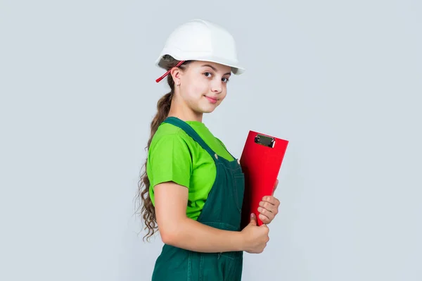 Especialista em segurança. criança usar capacete no canteiro de obras. adolescente construtor menina com documento de papel de construção. criança em trabalhos de reparação. conceito de renovação em oficina. ocupado carpinteiro profissional — Fotografia de Stock