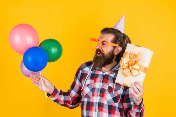 Snygg skäggig kille med trendig frisyr bära rutig skjorta hålla fest ballonger och presentförpackning, födelsedag — Stockfoto