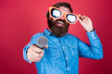Bunu dene. Mutlu gülümseyen olgun adam. Sakallı adam mikrofonda şarkı söylüyor. Vahşi Kafkas hipster etkinlik yöneticisi. Komik parti gözlükleri. Karaoke ve müzik. Mikrofonlu erkek hoparlör. vokal