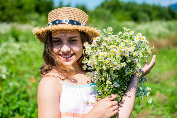 Happy kid with healthy baby skin smile with romomile flowers natural floral spa and beauty care in sun hat on sunny summer landscape, skincare — стоковое фото