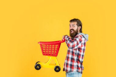 Şık bakımlı ve sakallı bir erkek hippi alışveriş arabası taşıyor, günlük rutin.