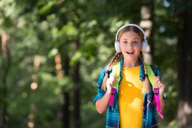 Tatlı çocuk modern kulaklıklarla müzik dinleyip yaz manzarasını geziyor açık hava, ses, fotokopi alanı.