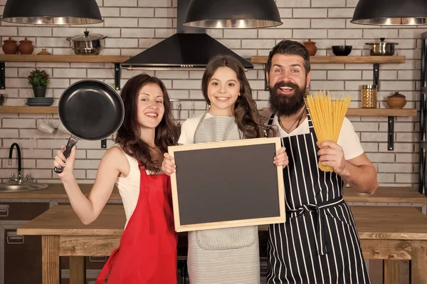 friendly family in kitchen. cooking healthy food at home. kid chef with her parents. dad and mom teaching daughter how to cook. happy family day. mutual assistance and support. copy space