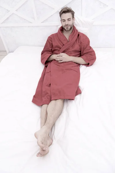 Att veta hur man slappnar av. Snygg man liggande i sängen för att slappna av efter bad. Sömnig kille i röd badrock tar sig tid att slappna av på morgonen. Det är dags att koppla av — Stockfoto