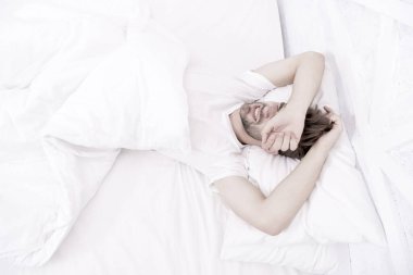 Beyaz yatak odasında uyuyan adam. Evde rahat bir hafta sonu. Rahatlama zamanı. Adam uykusuz bir gece geçirmiş. Erkek sağlığı konsepti. Barışseverlik kavramı. Yorgun adam yatakta uyuyor. Sabah erken kalktım.