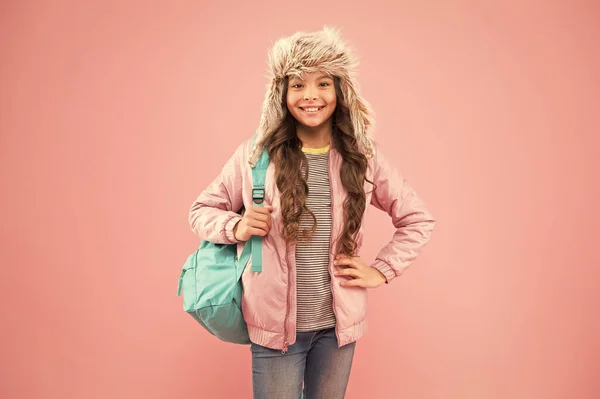 El final del año escolar. No más exámenes. Pequeña chica feliz de vuelta a la escuela. vacaciones de invierno y vacaciones. niño ropa de abrigo fondo rosa. sombrero de oreja niño feliz. colegiala con mochila ir a casa — Foto de Stock