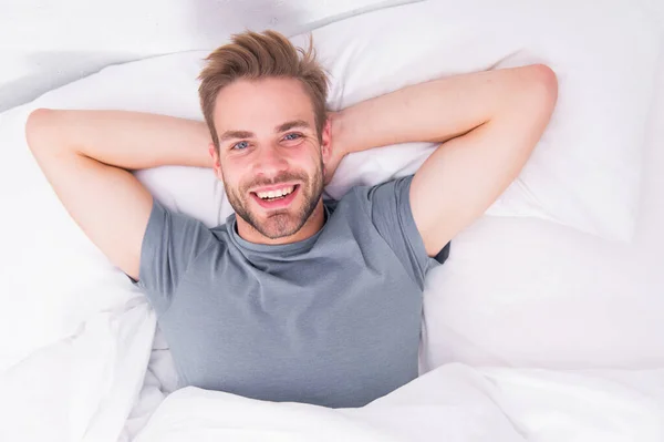 Novo sorriso, novo dia. Um homem feliz acorda na cama. Bonito homem caucasiano com sorriso feliz relaxante pela manhã. Tratamento de sorriso branco espumante e procedimento de pós-tratamento. Sorriso que se encaixa no seu estilo de vida — Fotografia de Stock