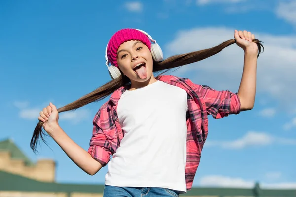 Chica divertida sobresalen lengua escuchando música y sosteniendo el pelo largo morena cielo soleado, cuidado del cabello — Foto de Stock