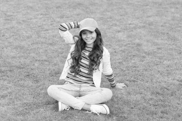 Su estilo en perfecto estado. Primavera día soleado. colegiala alegre relajarse en la hierba verde. pupila sonriente niño usar estilo casual. de vuelta a la escuela. Feliz día de los niños. niña pequeña al aire libre. moda para niños —  Fotos de Stock