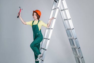 Kız çocuğu üniforma ve kask giyer atölyede çalışırken merdivende çekiçle, kariyerle